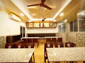 Un comedor con mesas y sillas, ventiladores de techo y una ventana con persianas.