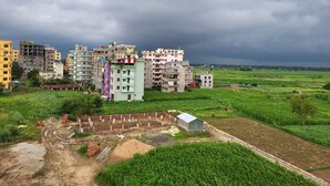 A residential area with multi-story buildings, a dirt road, and surrounding green fields.