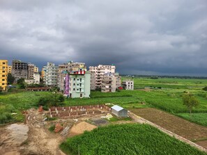 Una zona residencial con edificios de varios pisos, un camino de tierra y campos verdes circundantes.