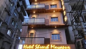 A multi-story hotel with a neon sign, a tiled entrance, and potted plants.