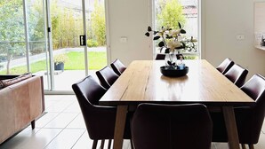 Un comedor con mesa y sillas de madera, ventanas amplias y vistas al exterior con vegetación.