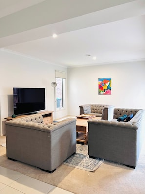 Uma sala de estar moderna com uma televisão de tela plana, dois sofás cinzas, uma mesa de centro e um abajur.