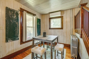 Una habitación con paredes de madera, una mesa con cuatro sillas, un radiador y una ventana que da a vistas de árboles.
