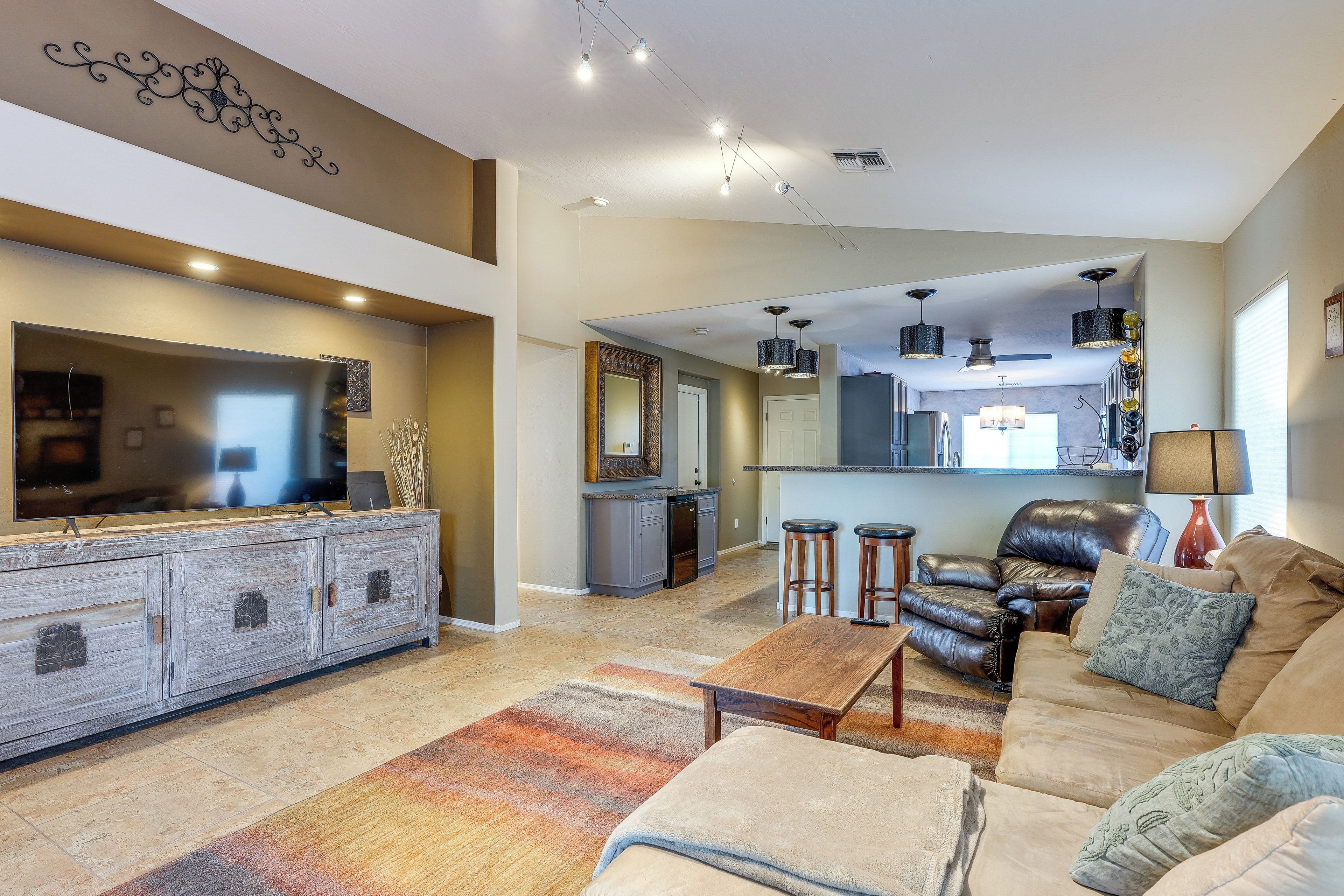 A spacious living room with a large flat-screen TV, a leather sofa, and a coffee table.