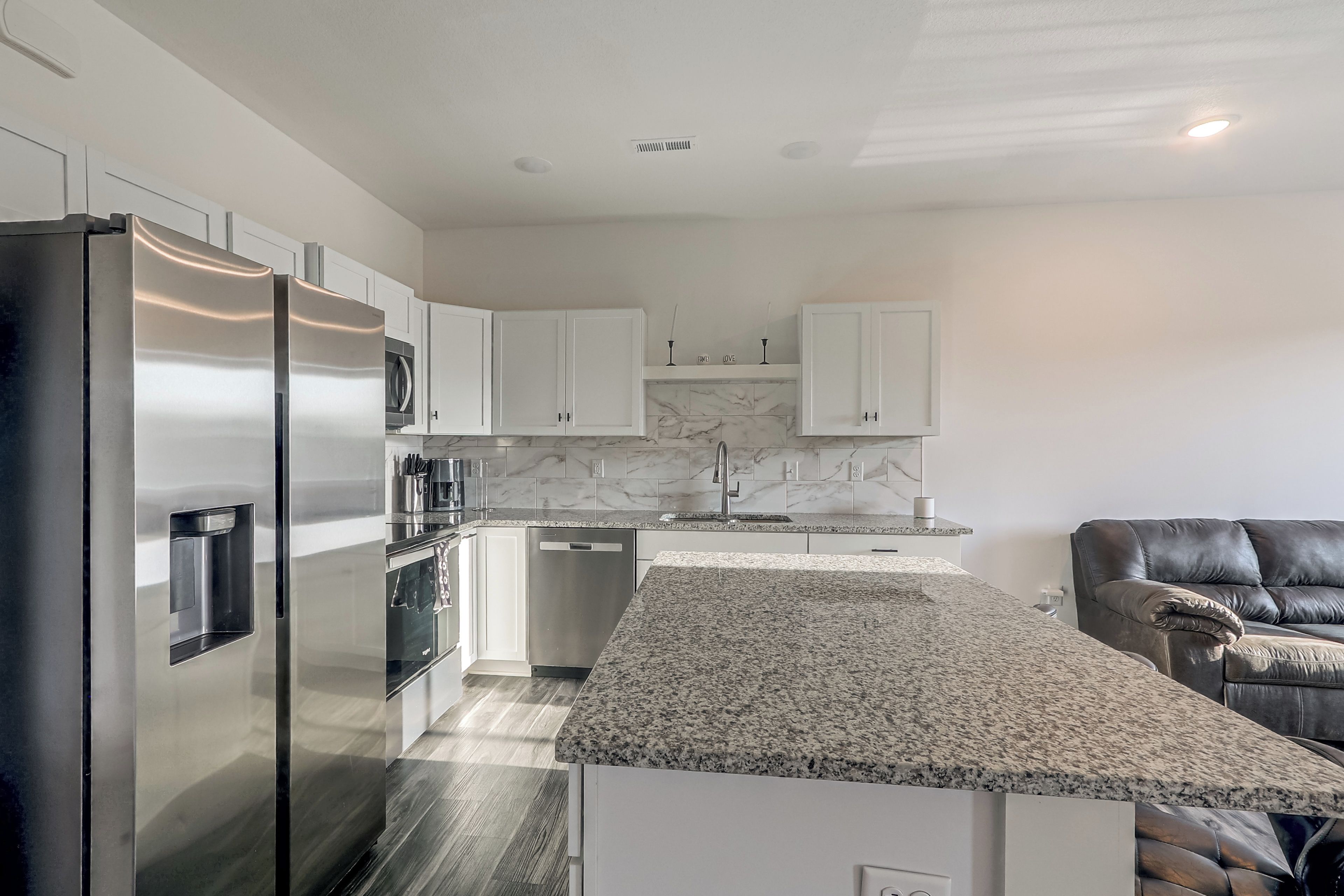 A modern kitchen with stainless steel appliances, white cabinetry, and a granite countertop.