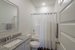 Une salle de bain avec un lavabo sur un plan de travail en granit, des toilettes, une douche avec un rideau et un miroir avec un cadre à motifs en chevrons.