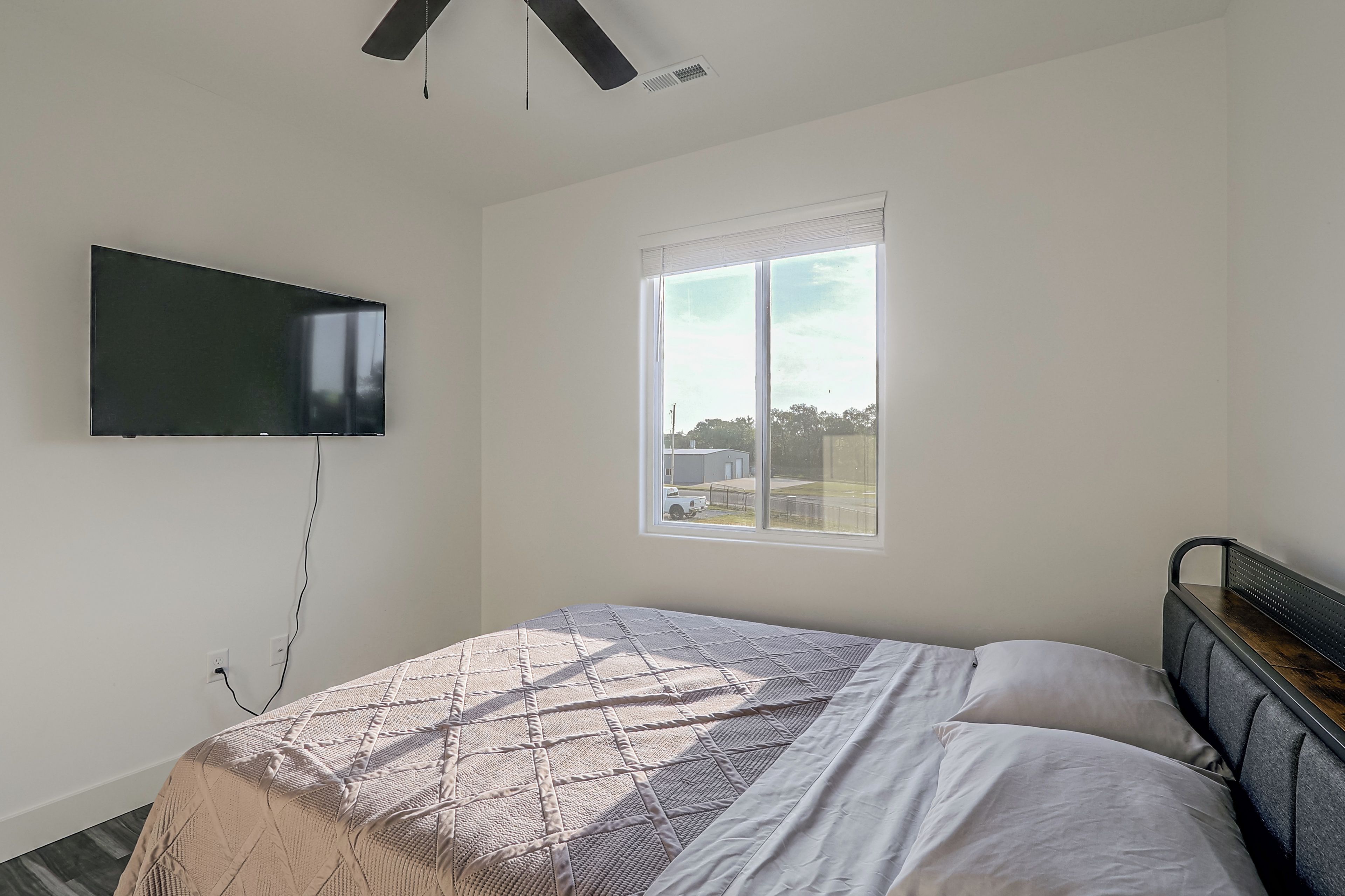 A bedroom with a bed, a TV mounted on the wall, and a window.