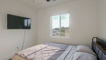 A bedroom with a bed, a TV mounted on the wall, and a window.