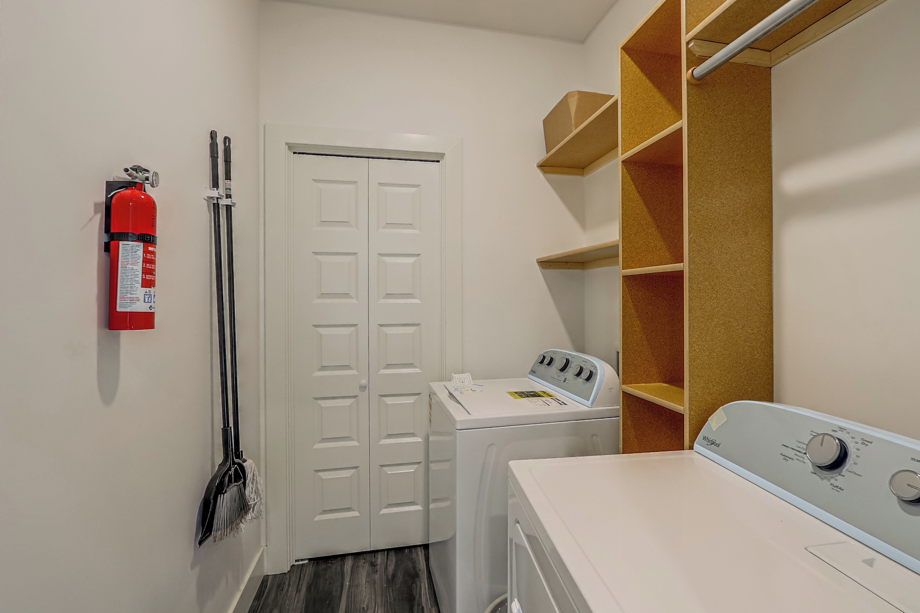 A laundry room with a washing machine, a dryer, a fire extinguisher, and a broom.