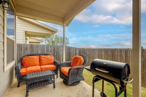 Eine überdachte Terrasse mit Korbmöbeln und einem Grill.