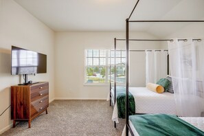 Ein Schlafzimmer mit Himmelbett, einem Fernseher auf einer Holzkommode und einem Fenster mit Jalousien.