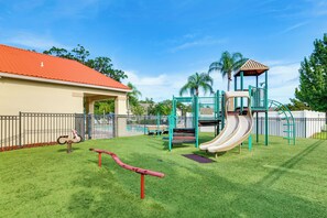 A playground with a slide and climbing structures, surrounded by a fence and grass. - Pool Access! Kissimmee Gem, Enclosed Patio (Kissimmee)
