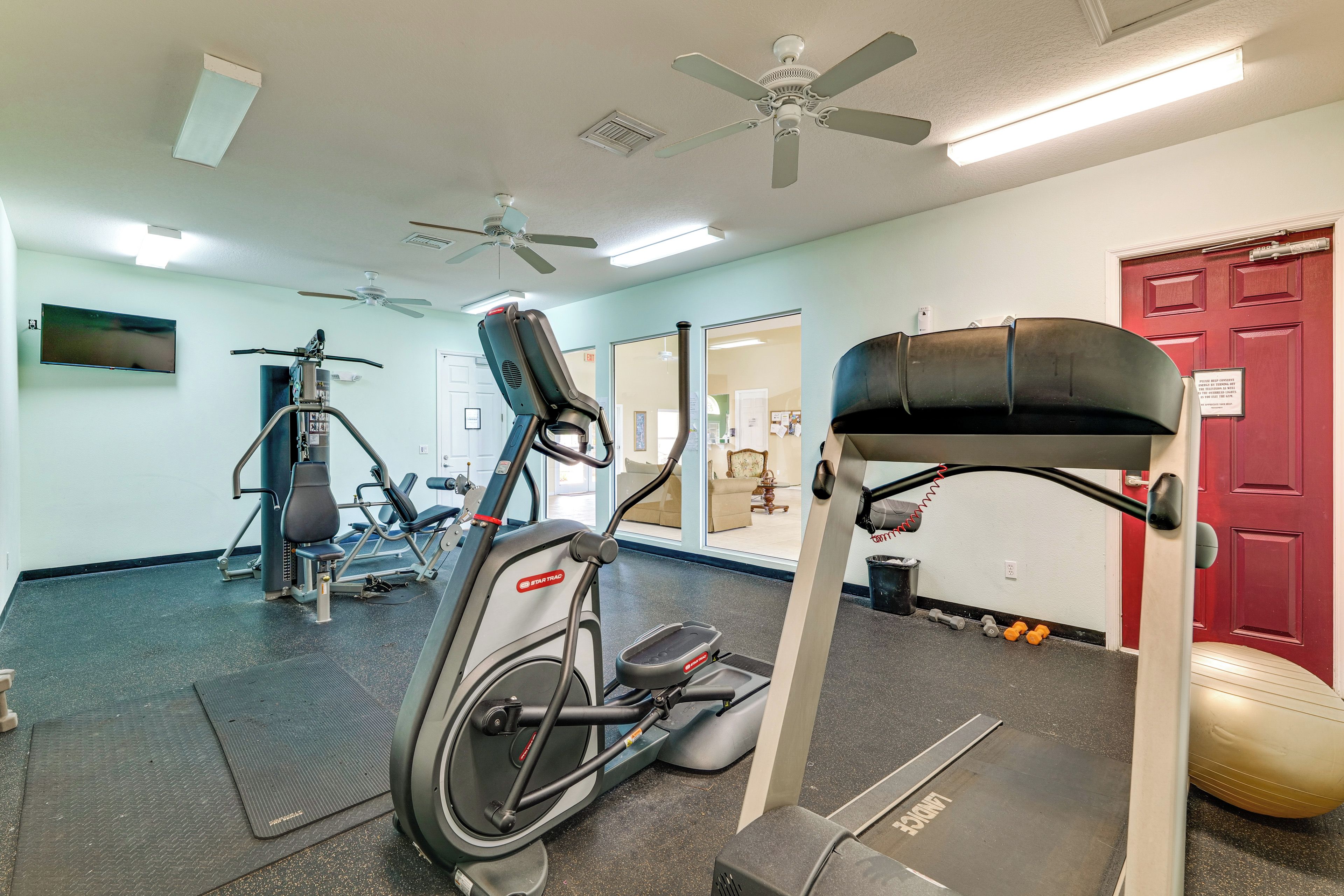 A gym with exercise equipment, a treadmill, and a red door.