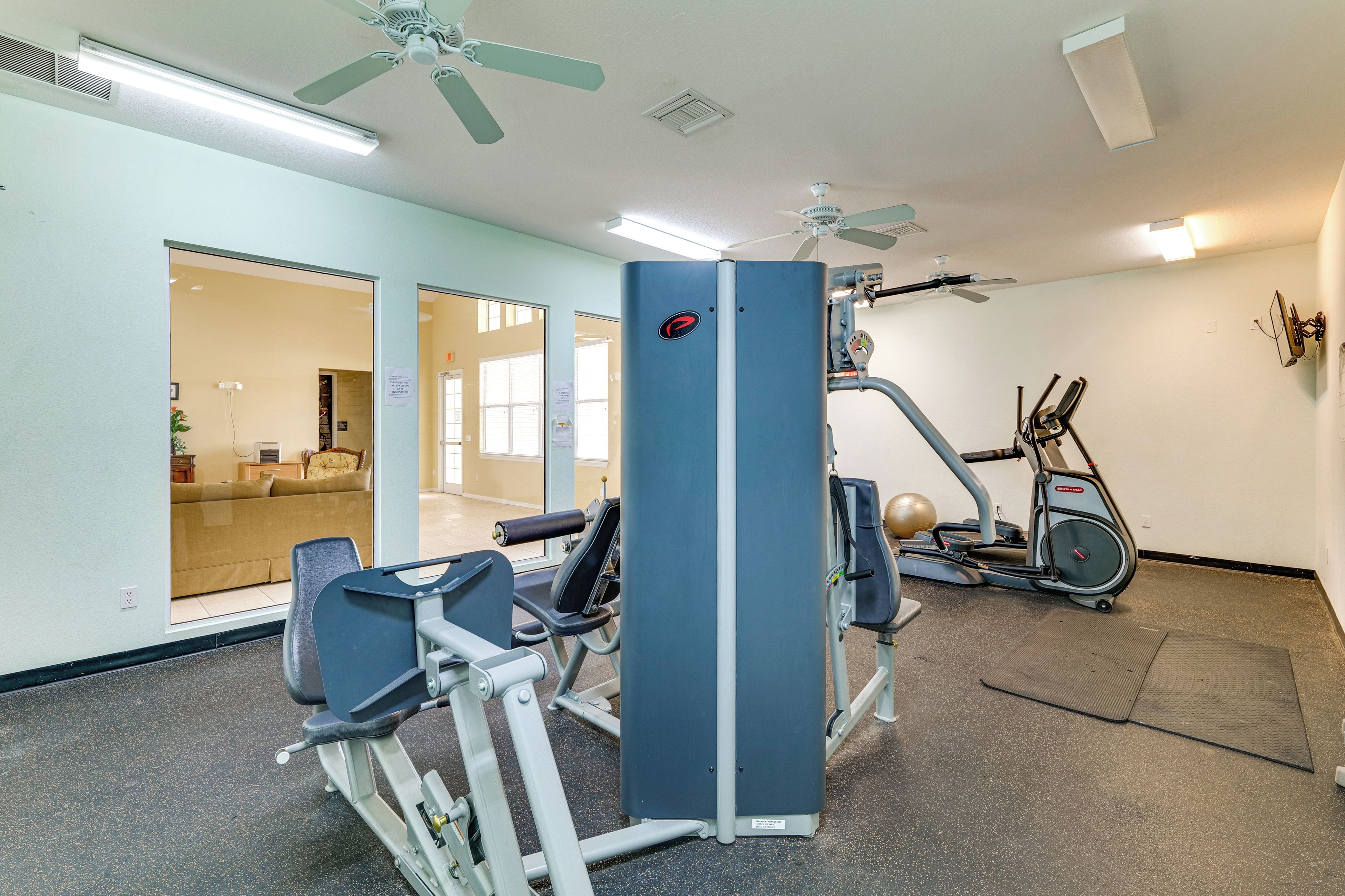 A gym with exercise equipment, a ceiling fan, and a door leading to a living area.