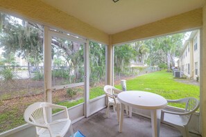A covered patio with a table and chairs, large windows, and a view of a grassy yard and buildings. - Pool Access! Kissimmee Gem, Enclosed Patio (Kissimmee)