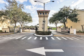 A gated entrance with a directional arrow on the road, a streetlight, and a tower-like structure. - Pool Access! Kissimmee Gem, Enclosed Patio (Kissimmee)