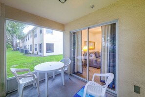 A covered patio with a table and chairs, a sliding glass door leading to an interior space with a lamp and furniture. - Pool Access! Kissimmee Gem, Enclosed Patio (Kissimmee)