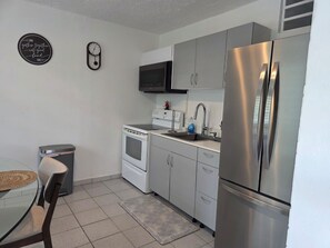 A compact kitchen with a stainless steel refrigerator, a microwave, and a stove. There is a small trash bin and a chair near the table. - Charming 3-Bedroom House in Monte Vista Fajardo, Puerto Rico (Fajardo city)
