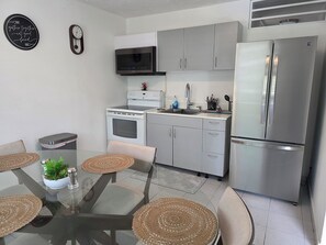 A modern kitchen with stainless steel appliances, a dining table with woven placemats, and a clock on the wall. - Charming 3-Bedroom House in Monte Vista Fajardo, Puerto Rico (Fajardo city)