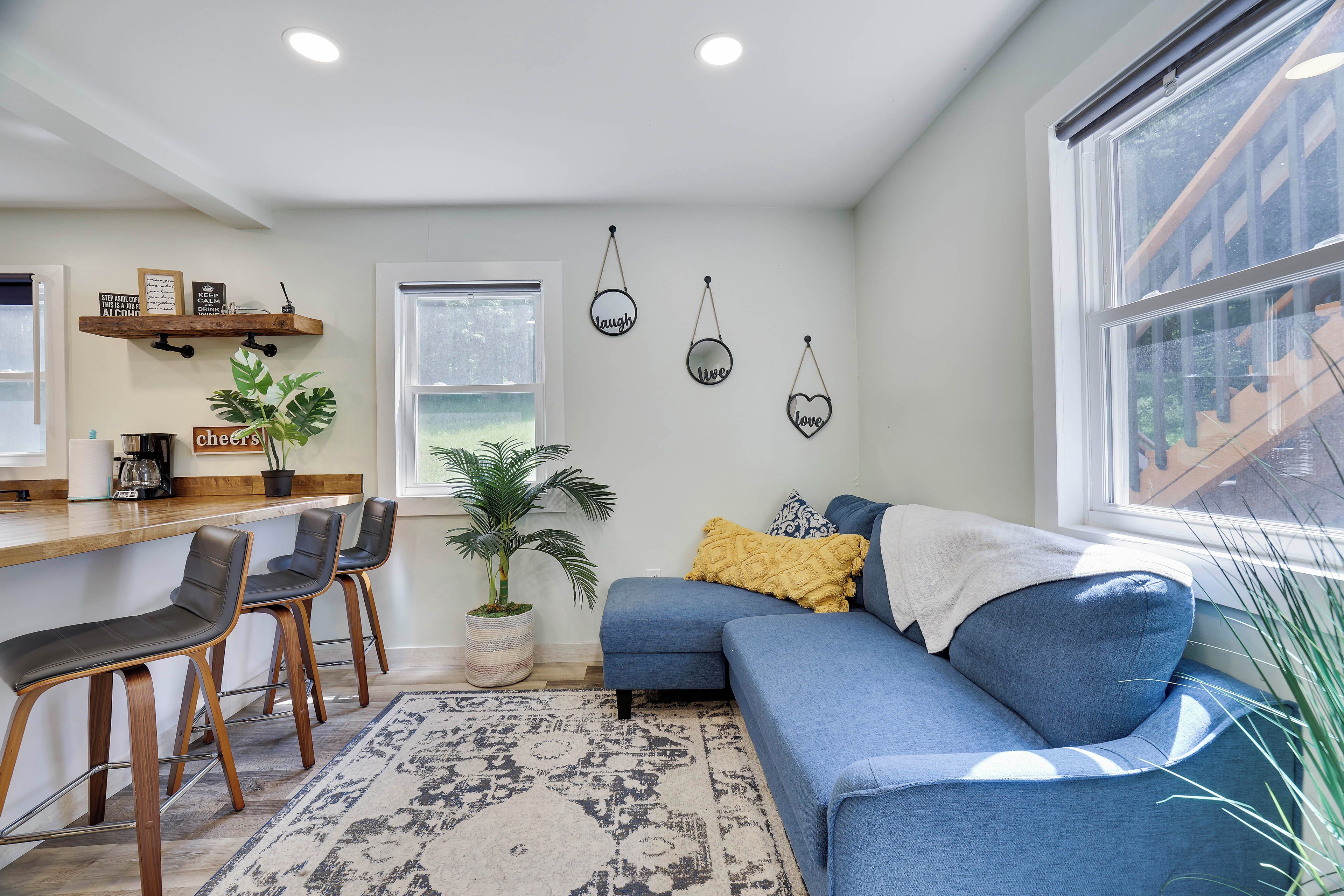 A modern living room with a blue sofa, a coffee table, and a dining area with chairs and a bar.