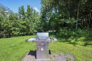 Una parrilla comercial Char-Broil en un área verde al aire libre con árboles al fondo.