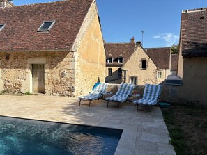 A stone building with a swimming pool and lounge chairs.