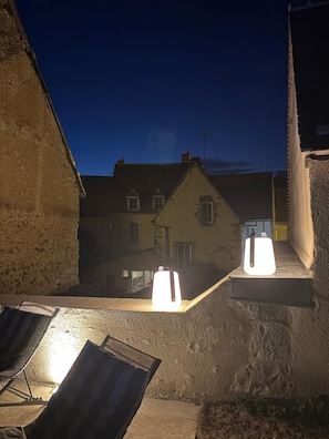 A nighttime view of a narrow alleyway with buildings on either side. There are two illuminated objects on the ledge, possibly outdoor lights or speakers.