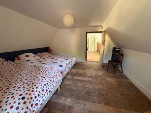 Ein Schlafzimmer mit zwei Betten, einem Holzstuhl, einem Heizkörper und einer Tür zu einem Flur.