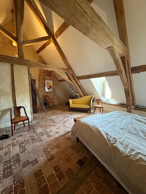A room with exposed wooden beams, a brick wall, a bed, two chairs, and a yellow sofa.
