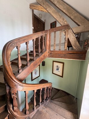 Eine Wendeltreppe aus Holz mit Handlauf und einer Zwischenebene mit gerahmten Kunstwerken.
