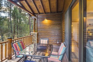 A wooden deck with a glass table and chairs, surrounded by a wooden railing and a stone wall. - Torreon Mountain Retreat - Golf, Hike, Relax (Show Low)