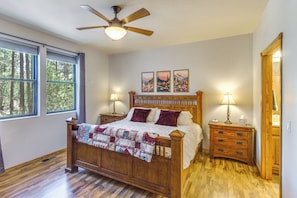 A bedroom with a wooden bed, two bedside tables, a ceiling fan, and a window with a view of trees. - Torreon Mountain Retreat - Golf, Hike, Relax (Show Low)