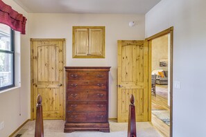 A room with a wooden dresser, two doors, a window with a red curtain, and a ceiling-mounted smoke detector. - Torreon Mountain Retreat - Golf, Hike, Relax (Show Low)