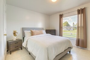 Une chambre à coucher avec un lit, des tables de chevet, une commode et une fenêtre avec des stores.