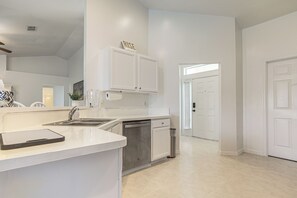 Une cuisine moderne avec des meubles blancs, un lave-vaisselle encastré et un grand îlot central doté d’un évier.
