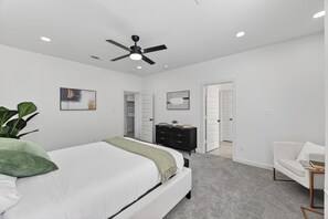 A modern bedroom with a bed, a ceiling fan, a dresser, and a chair. - Houston Retreat: Gated Community Near the Galleria (Houston)