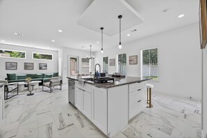 A modern kitchen with a central island, white cabinetry, and a dining area with a green sofa. - Houston Retreat: Gated Community Near the Galleria (Houston)