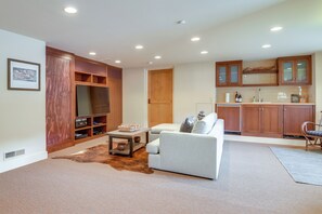 Ein Wohnzimmer mit einer Couch, einem Couchtisch und einem Fernseher. Es gibt eine Küchenzeile mit Holzausbau und einer Arbeitsplatte.