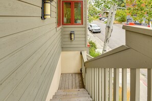 Eine hölzerne Treppe führt zu einem Balkon mit einem roten Fensterrahmen und einer Wandleuchte.