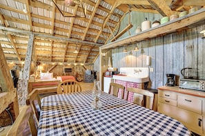 Un interior rústico de madera con una mesa de cuadros, una cama, una zona de cocina con un lavabo y un tostador, además de una guitarra.