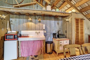 Una cocina rústica con un lavamanos, un microondas, un tostador y una silla de madera.