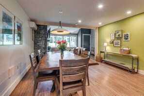 A dining area with a wooden table and chairs, a vase with flowers, and a stone wall. - Stowe Ski, Bike & Hike Condo w/ Pools & Clubhouse (Stowe)