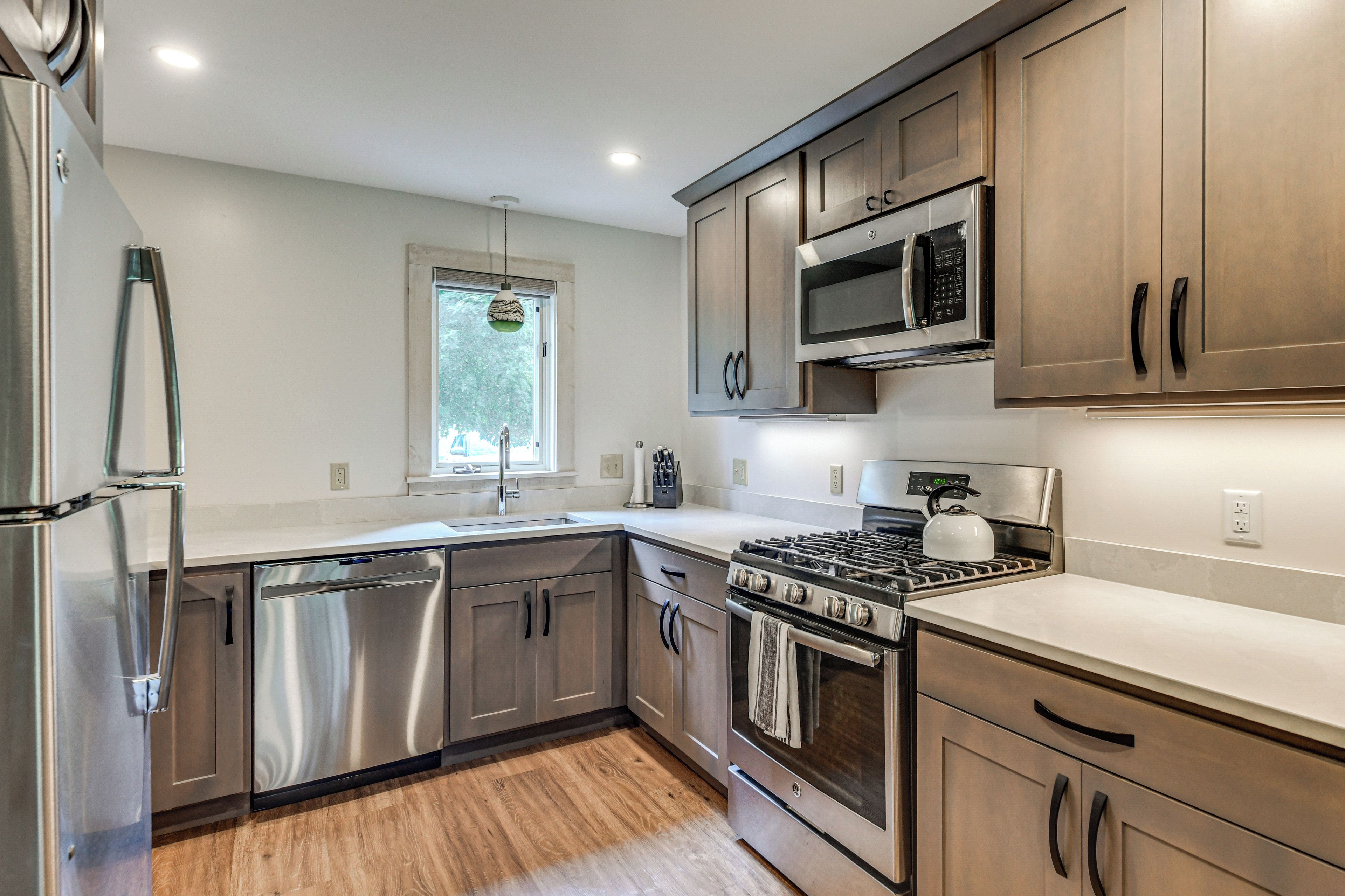 A modern kitchen with stainless steel appliances, wooden cabinets, and a window with a view of trees.