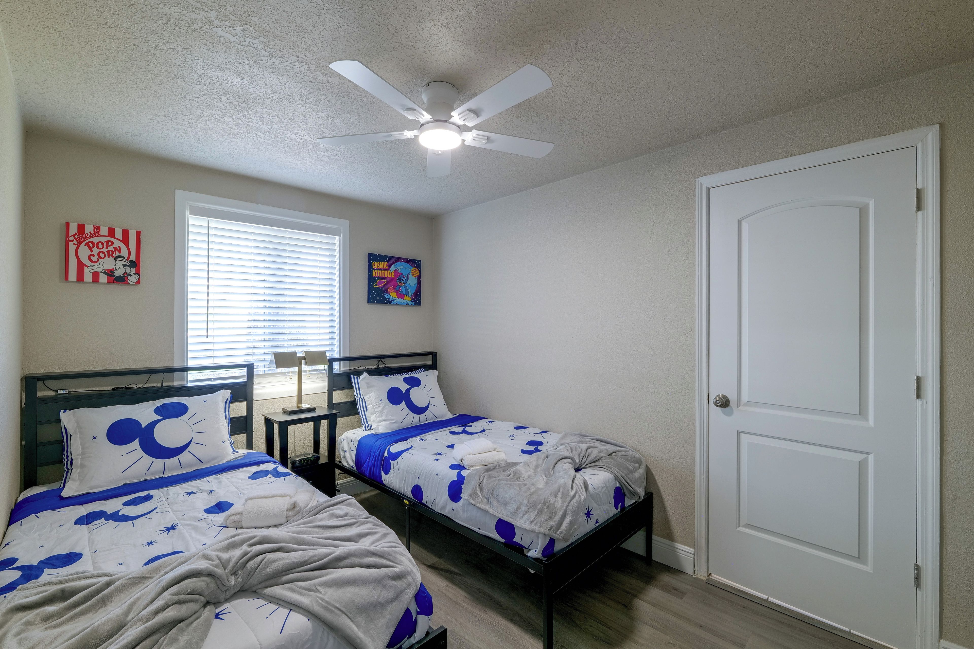 Une chambre avec deux lits, un ventilateur de plafond, une fenêtre avec des stores et une porte.