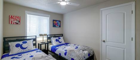 Un dormitorio con dos camas, ventilador de techo, ventana con persianas y una puerta.