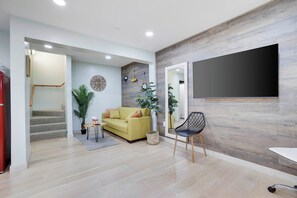 Un saló modern amb un sofà, una taula de centre i un televisor fixat a la paret. Hi ha una escala que porta a una altra habitació.