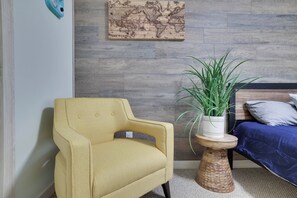A room with a yellow armchair, a wooden side table with a plant, a bed with blue bedding, and a world map on the wall. - Tannersville Mtn Escape: Ski, Hike & Shop! (Tannersville)