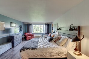 Un dormitorio con una cama grande, una silla roja, un escritorio y un ventanal con cortinas.