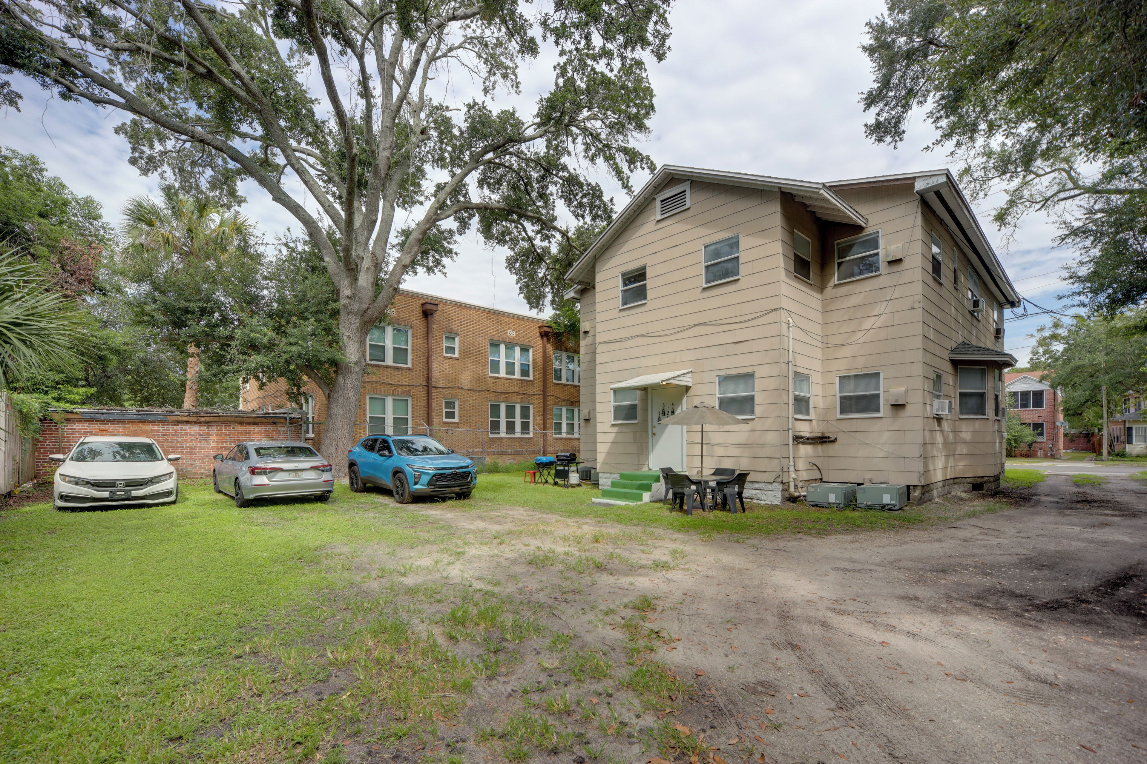 A two-story building with a brick facade, a front porch with a table and chairs, and a dirt driveway.