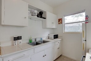A kitchen with white cabinets, a stainless steel sink, a microwave, and a window with a view of trees. - Stroll to Arts & Eats! Jacksonville Condo (Jacksonville)